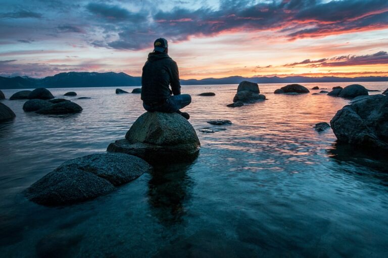 man sitting on rock in ocean at sunrise setting goals